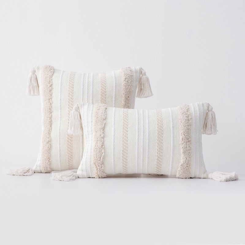 Three rectangular boho-style cushion covers with tufted detailing and tassels, in natural white and beige colours, displayed against a neutral background.