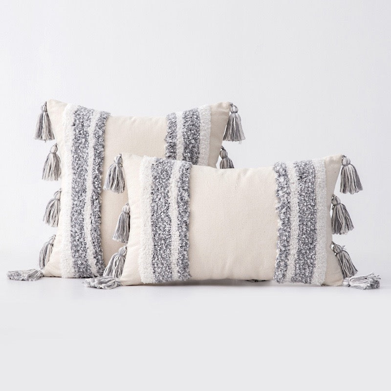 Three rectangular boho-style cushion covers with tufted detailing and tassels, in natural grey and beige colours, displayed against a neutral background.