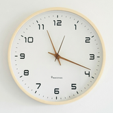 Round wall clock with beige frame and black numbers on a light gray background